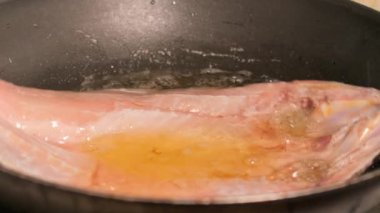 Mutfakta siyah bir tavada kızarmış levrek.