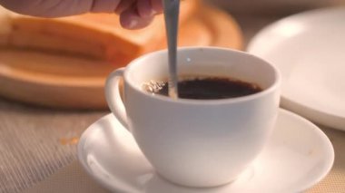 Sıcak kahveyi beyaz bardakta karıştırmak ve ekmeği kızarmış ekmeğe karıştırıp kahvaltı hazırlamak..