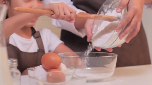 亚洲小女孩用铲子把母亲放在另一个搅拌碗里的杯子里的面粉刮成粉 做成自制的糕点 — 图库视频影像