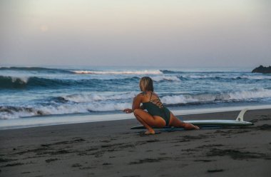 Genç kadın sörf yapmadan önce plajda germe yapıyor, Bali