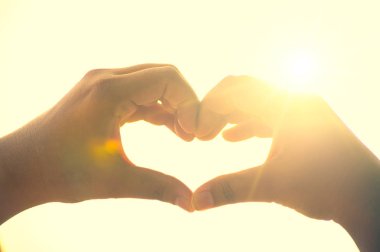 Kadın ve erkeğin elleri kalp şeklindedir. Güneş ışığı ellerden geçer.