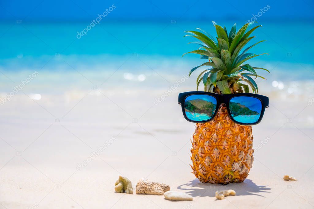 Glasses pineapples are located on the beach by the sea in the hot sun, setting the concept for summer.