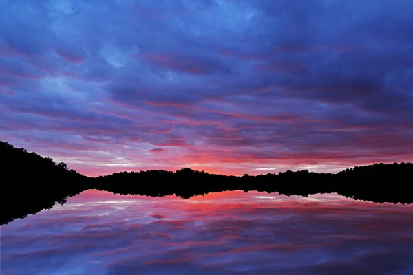 Landscape at twilight, shoreline of West Lake with mirrored reflections in calm water, Michigan, USA