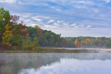 Derin Göl kıyılarının sisli sonbahar manzarası benzersiz bulutlar ve sakin sulardaki yansımalarla, Yankee Springs State Park, Michigan, ABD