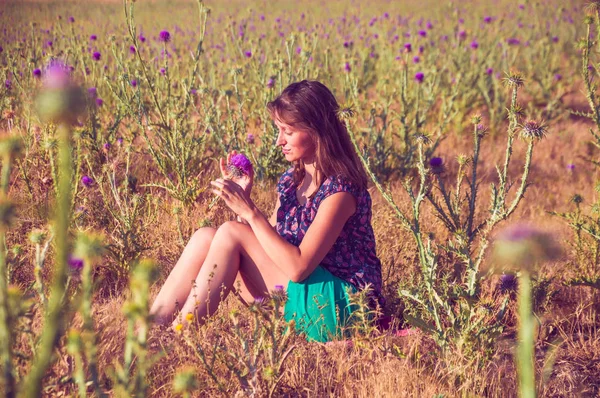 Romantic woman sitting in the field with a flower — Stock Photo, Image
