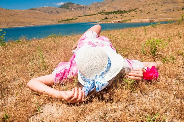 乾いた草の上に横たわる麦わら帽子の女性 — ストック写真