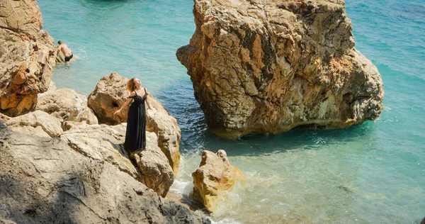 Young woman in black dress standing on the rocks — Stock Photo, Image