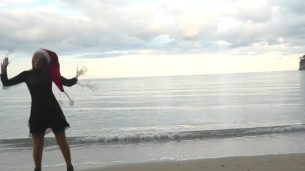 Забавная женщина в шляпе Санты прыгает возле моря — стоковое видео