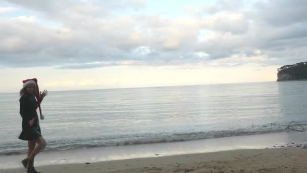 Забавная женщина в шляпе Санты, гуляющая по морю. — стоковое видео