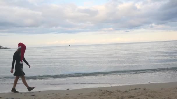 Frau mit Weihnachtsmütze geht traurig am Meer entlang — Stockvideo