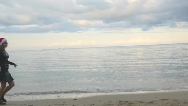 Αστεία γυναίκα σε Σάντα καπέλο αστείο περπάτημα δίπλα στη θάλασσα — Αρχείο Βίντεο
