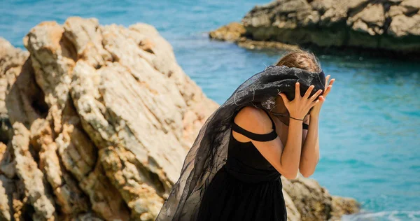 黒いスカーフを持つ黒のドレスの若い女性が岩の上に立って — ストック写真