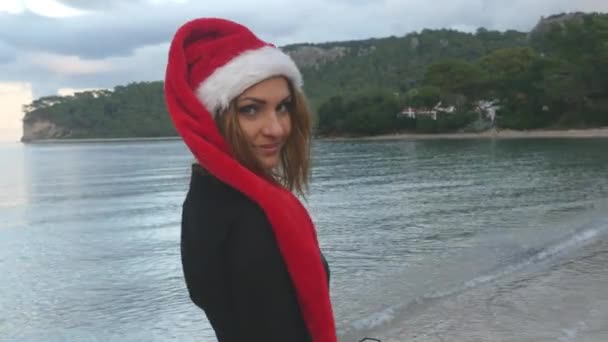 Junge Frau mit Weihnachtsmannhut am Meer — Stockvideo