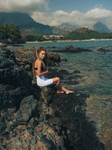 Mujer joven con rastas sentada en las rocas —  Fotos de Stock