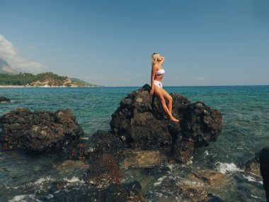 Genç bir kadın denizdeki kayalarda oturuyor.