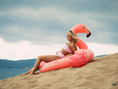 Plajdaki şişme flamingoda yatan genç kadın.