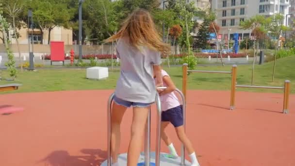 Två systrar leker på karusellen. — Stockvideo