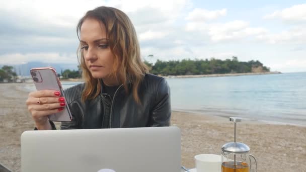Mujer joven que trabaja en el ordenador portátil y el uso de teléfono móvil en el café al aire libre — Vídeo de stock