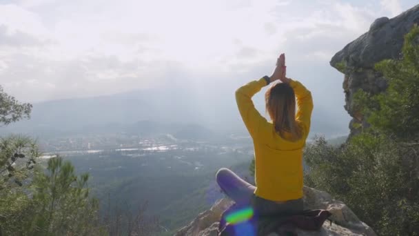 Молодая женщина, сидящая в позе йоги на конце утёса — стоковое видео