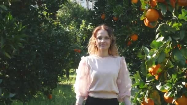 Jonge vrouw loopt in oranje tuin ruikend naar fruit — Stockvideo
