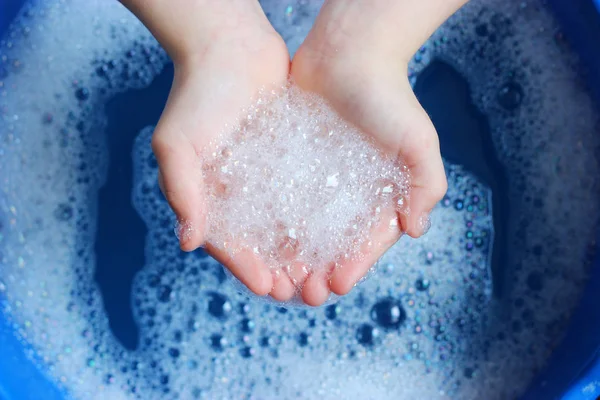 soap foam in the hands of the child on a beautiful blue background. Hand hygiene. Children\'s hygiene.