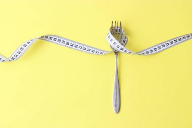 santimetre teyp ve metin eklemek için bir yer ile renkli bir arka plan üzerinde çatalı. minimalizm kompozisyon tarzı. Sağlık, kilo kaybı, diyet, doğru beslenme kavramı.
