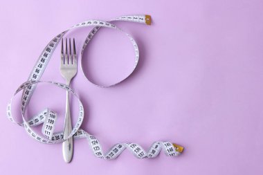 santimetre teyp ve metin eklemek için bir yer ile renkli bir arka plan üzerinde çatalı. minimalizm kompozisyon tarzı. Sağlık, kilo kaybı, diyet, doğru beslenme kavramı.