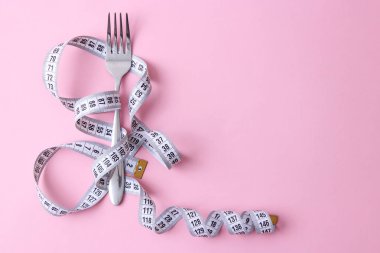 santimetre teyp ve metin eklemek için bir yer ile renkli bir arka plan üzerinde çatalı. minimalizm kompozisyon tarzı. Sağlık, kilo kaybı, diyet, doğru beslenme kavramı.