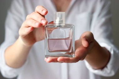 Kız bir şişe parfüm hafif bir arka plan üzerinde tutuyor. kadınsı koku. minimalizm. metin için yer.