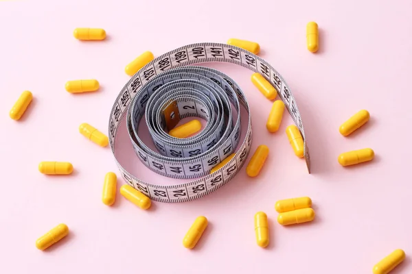 centimeter tape and pills on a colored background with space for text. concept of losing weight, diet, fat burning, healthy eating. minimalism.