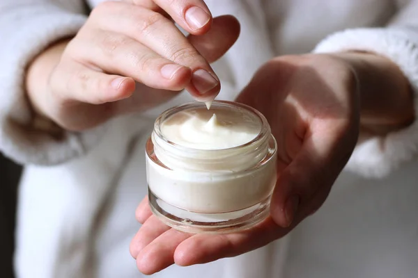 a girl in a bathrobe holds a jar with a cosmetic cream in her hands. skin care, minimalism. keep youth and skin elasticity.