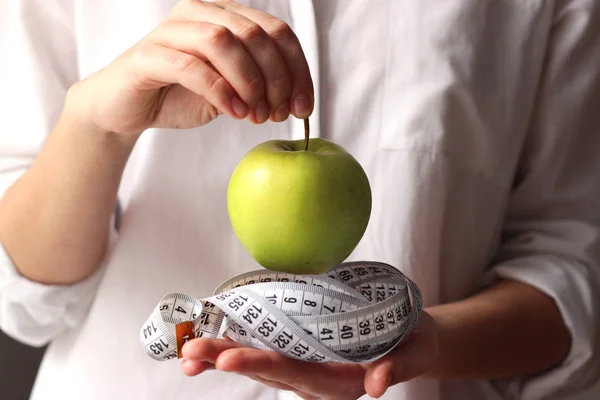 centimeter tape and a green apple in female hands on a light background. minimalism, diet, fitness, healthy nutrition, vitamins. Concept of health, body.