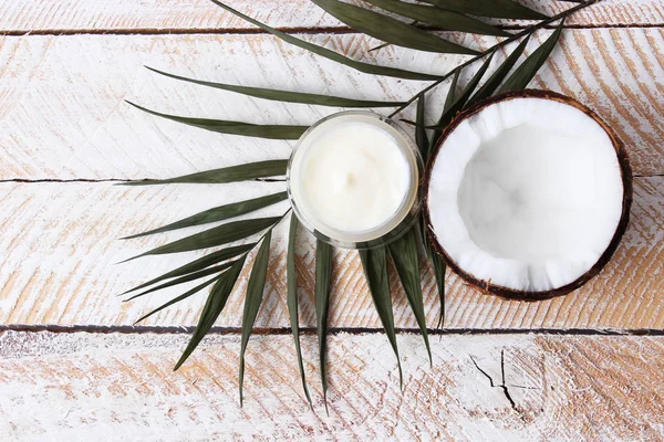 Cosmetic natural skin care products from coconut. palm leaf, coconut and cosmetic cream on a wooden background. minimalism, the top. flatlay