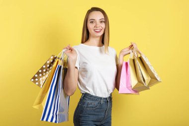 Renkli bir arka planda alışveriş yapmak için kağıt torbaları olan güzel bir genç kız.