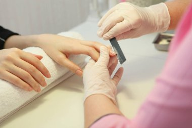 Tırnak törpüsü takan bir kozmetik uzmanı tarafından manikür yaptıran bir kadının yakın çekimi. Kadın manikür yaptırıyor. Güzellik uzmanı müşteriye çivi çakıyor..