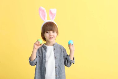 Elinde Paskalya yumurtaları ve kafasında renkli bir arka planda tavşan kulakları olan sevimli bir çocuk. Metin eklenecek yer ile paskalya arkaplanı.