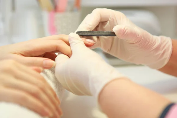 Closeup shot of a woman in a nail salon getting a manicure by a cosmetologist with a nail file. Woman gets a manicure of nails. Beautician puts nails on the client.