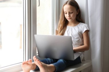 Küçük tatlı kız modern bir dizüstü bilgisayar üzerinde çalışıyor..