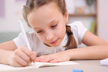 Şirin küçük kız odanın içinde ödev yapıyor..