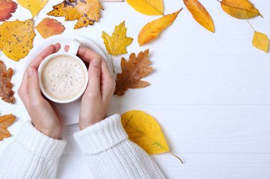 Sonbahar kompozisyon üst görünümü. Ellerde ve sonbahar yapraklarında bir fincan kahve