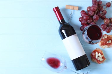 Masanın üstünde kırmızı şarap ve atıştırmalıklar var. Şarap, prosciutto, peynir, baget, üzüm, bal.