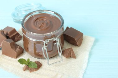Renkli bir arka planda cam kavanozda çikolata ezmesi. Çikolata yağı, çikolata sosu..