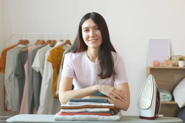 Genç ev hanımı odanın içinde giysileri ütülüyor..