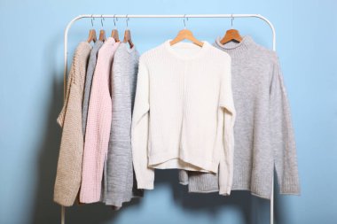 Renkli bir arka planda, gardırop askısında sıcak kazaklar. Sonbahar, kış giysileri..