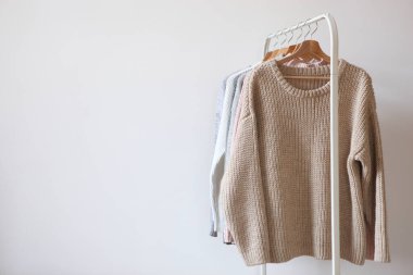 Hafif arka planda gardırop askısında sıcak süveterler. Sonbahar, kış giysileri..