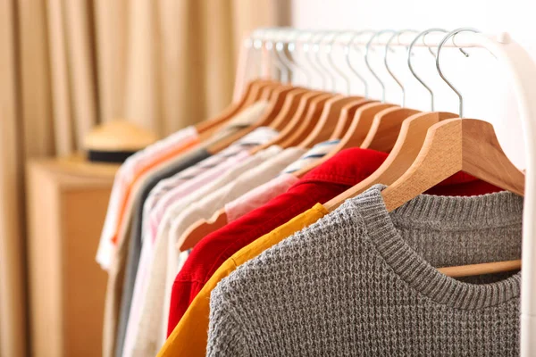 Fashionable clothes on hangers on a wardrobe rack in the background of the room.