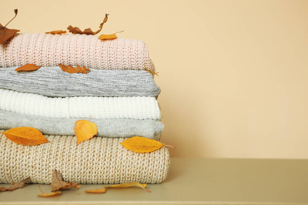 A stack of warm sweaters and autumn leaves on the table.