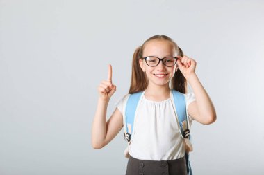 Sırt çantası ve arka planda kırtasiyesi olan neşeli bir okul kızının portresi. Mesaj için yer. Okula dönelim. Okul hazırlıkları. Ulusal Okul Sırt Çantası Farkındalık Günü.
