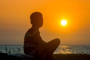 Sakat bir çocuk nehirde oturup gün batımını seyrediyor. Hüzünlü bir günün sonu.