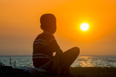 Sakat bir çocuk nehirde oturup gün batımını seyrediyor. Hüzünlü bir günün sonu.